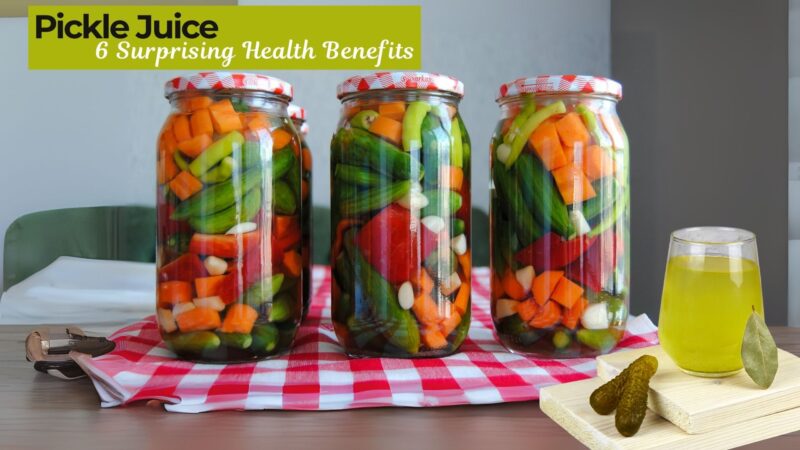 A glass of pickle juice next to fresh cucumbers and pickles